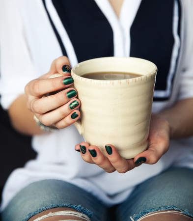 Stylish fashionable girl with a Cup of coffee and a green manicure in jeans. Fashion, care, beautyの写真素材