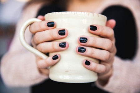 girl hands holding a cup of coffee with beautiful black manicure. Christmas