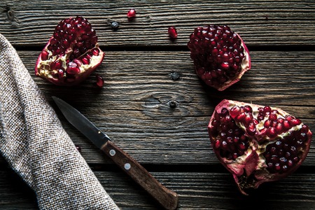 Ripe pomegranates, napkin and table knife on white wooden background