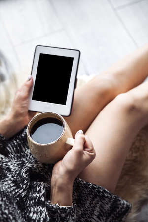 beautiful stylish girl in leather trousers and a modern sweater sitting on the floor with a cup of coffee and mobile phoneの写真素材