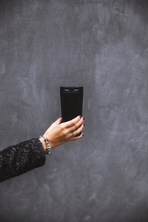 girl with beautiful manicure hand holding a black vacuum tumbler on a gray background a