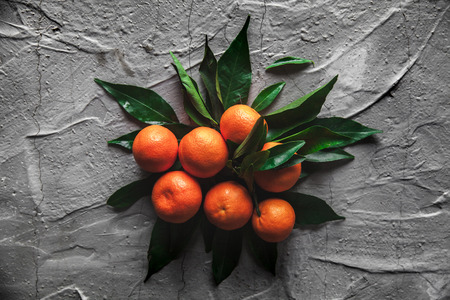 Tangerines (oranges, mandarins, clementines, citrus fruits) with leaves on gray cement background. Organic vegetarian food. Winter local fruits. Healthy detox eating concept. Copy space.の写真素材