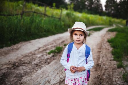 Little beautiful girl in hat and backpack in natureの写真素材