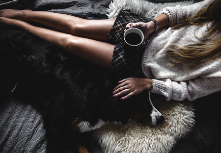 Beautiful girl lying and her cute dog Bernese Mountain Dog on bed, Stylish, fashionable, cozyの写真素材