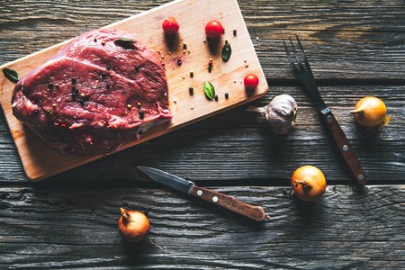 Meat with spices and vegetables on wooden background. Knife. food a