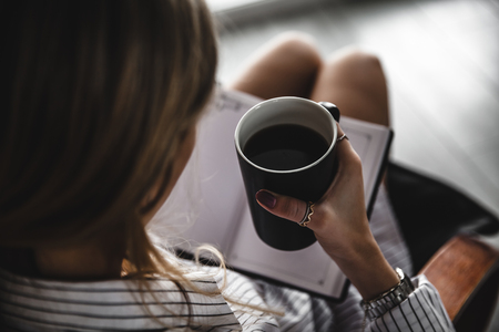 Woman on the chair with old book and cup of coffee aの写真素材