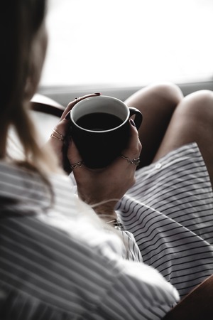 Female hands holding a white cup of tea, burgundy manicure, the girl is dressed in a shirt aの写真素材