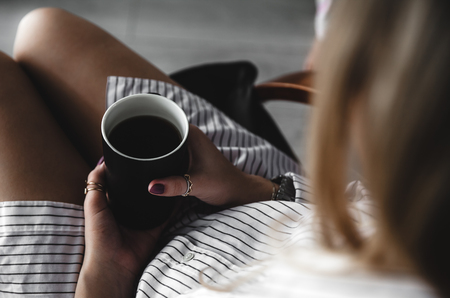 Female hands holding a white cup of tea, burgundy manicure, the girl is dressed in a shirtの写真素材