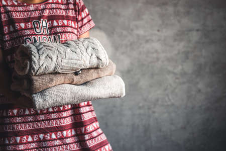 A girl in a Christmas dress holds a stack of sweaters. Warmth, comfortの写真素材