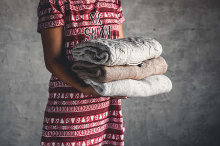 A girl in a Christmas dress holds a stack of sweaters. Warmth, comfortの写真素材