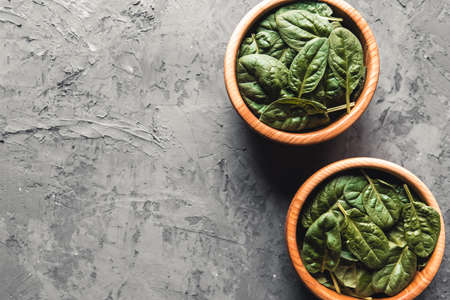 Baby spinach leaves in bowl on grey concrete background. Clean eating, detox, diet food ingredient