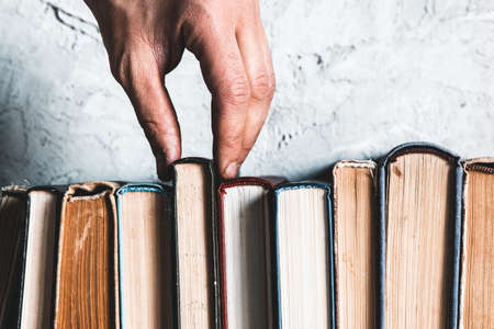 Male hand holding a book of bookshelves. Education, reading, hobbiesの写真素材