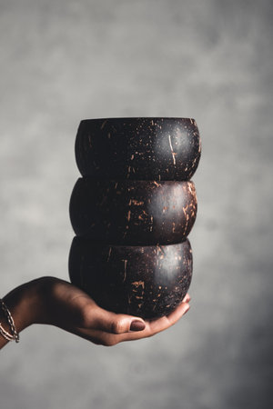 A stack of coconut bowls in the woman's hands. Natural tableware on a gray background.の写真素材