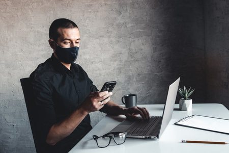 A masked man works at a computer. Pandemic, coronavirus, epidemicの写真素材