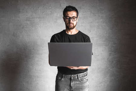 Man in a black T-shirt with a laptop on a gray background. Education, success, knowledge aの写真素材