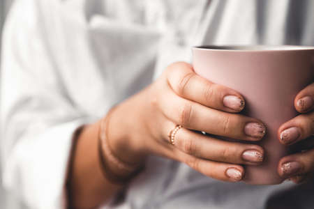 Woman in a white t-shirt holds morning coffee in a pink ceramic cup. Manicure. Front viewの写真素材