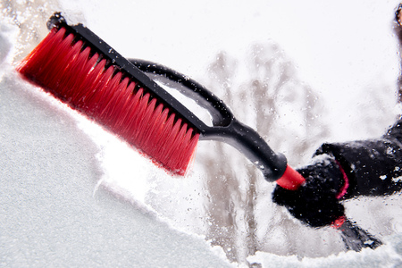 women hand in black glove removes snow from car windshield in winter dayの写真素材