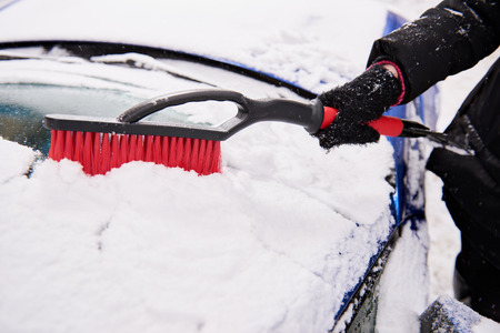 women hand in black glove removes snow from car windshield in winter dayの写真素材