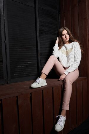 Portrait of beautiful woman in pink pants and white sweater on the brown wallの写真素材