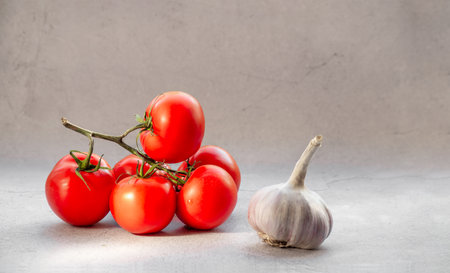 Fresh tomatoes on a vine with garlic on a light background.の写真素材