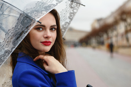 Portrait of young beautiful girl hiding under an umbrella from a small rain. View of the model is...