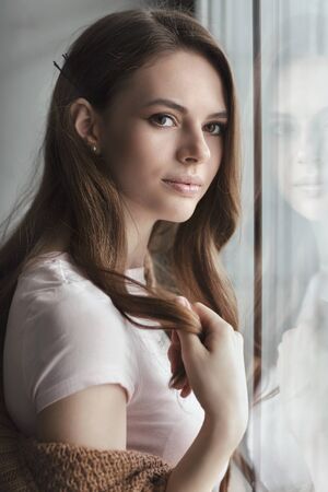 Young beautiful girl looks out the window. Close-up portraitの写真素材