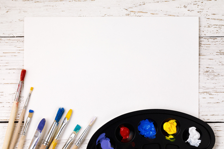 Artistic accessories: a palette with paints and tassels for drawing on a wooden table with space for textの写真素材
