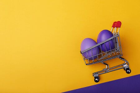 Multicolored easter eggs in a grocery cart with space for text. Holiday ingredients on a yellow...