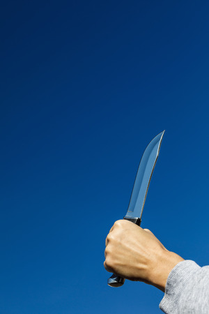 Hand with knife on blue sky background with copy spaceの写真素材