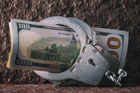 Dollars in handcuffs close-up. Concept on the limitation of currency circulation in different countriesの写真素材