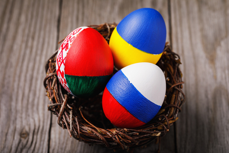 Three Easter eggs painted in colors of the flags of Ukraine, Belarus and Russia in the nestの写真素材