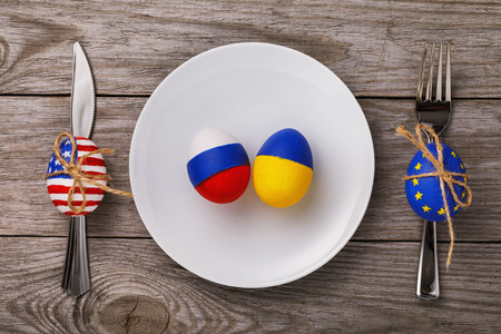 Two Easter eggs painted in the color of the flags of Russia and Ukraine in a plate on a wooden...