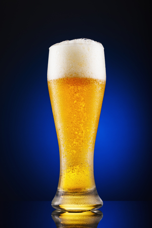 Full glass of freshly poured beer on a blue backgroundの写真素材
