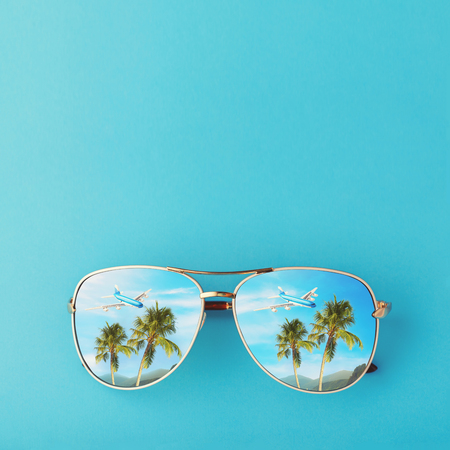 Sunglasses with palm trees, a plane and mountains reflected in them. Concept on the theme of vacation and travel with copy spaceの写真素材