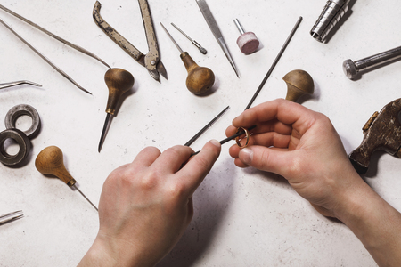 The jeweler is engaged in repairing the gold ring at his workplace. Top view of the workflowの写真素材