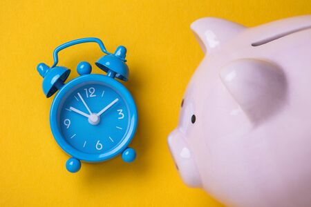 Alarm clock and moneybox on the table, top view. Time to save money