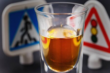 Concept on the topic of driving while intoxicated. Glass of whiskey and traffic signs. Human weakness and social securityの写真素材