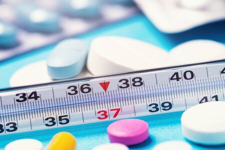 Thermometer with a temperature of 36.6 degrees, surrounded by various tablets, close-upの写真素材