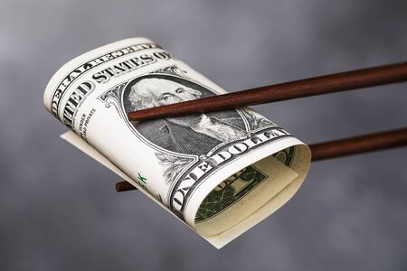 Chinese chopsticks hold one dollar, closeup. A concept on the relationship between America and Chinaの写真素材