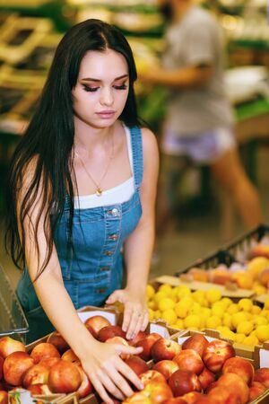 Young girl chooses peaches in a supermarketの写真素材