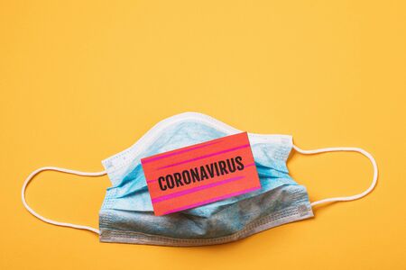 Medical disposable mask and a sheet of paper with the inscription coronavirus on a yellow background with copy space. 2019-nCoV Dangerous Pneumonia Outbreak Conceptの写真素材