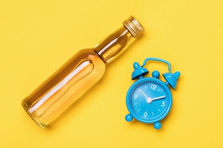 Bottle of whiskey and watch on a yellow background, top view. Concept on the topic: how long does alcohol hold in the blood of a personの写真素材