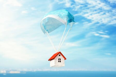 A toy house flies on a parachute from a medical mask. The concept of a protected house from virusesの写真素材