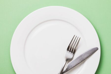 Empty white plate and cutlery on a green background, top viewの写真素材