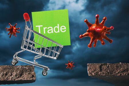 A grocery cart with a note falling from a cliff and a toy coronavirus against a stormy sky. Concept on the fall of trade due to the pandemic covid-19の写真素材