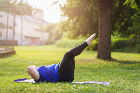 Young blonde size plus performs exercises for abdominal muscles in the park. The concept of a healthy lifestyleの写真素材