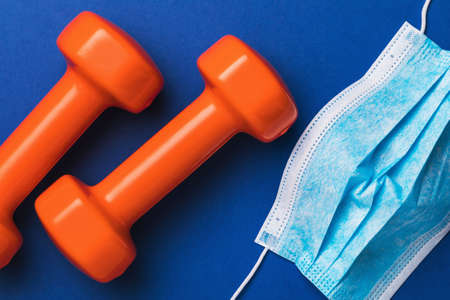 Dumbbells and disposable medical mask on a blue background. Concept on the topic of wearing masks in sports clubsの写真素材
