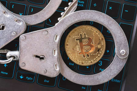 Handcuffs and bitcoin on a laptop keyboard, top view. Concept on the topic of punishment for mining digital currencyの写真素材