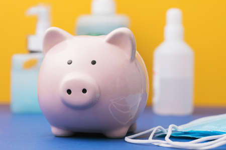 Piggy bank and personal protective equipment on the table. Concept on the topic of spending on hygiene products during a pandemicの写真素材