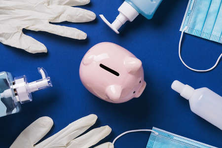 Pink piggy bank and medical supplies on a blue background, top view. Concept of spending on personal protective equipment during the COVID-19 pandemicの写真素材